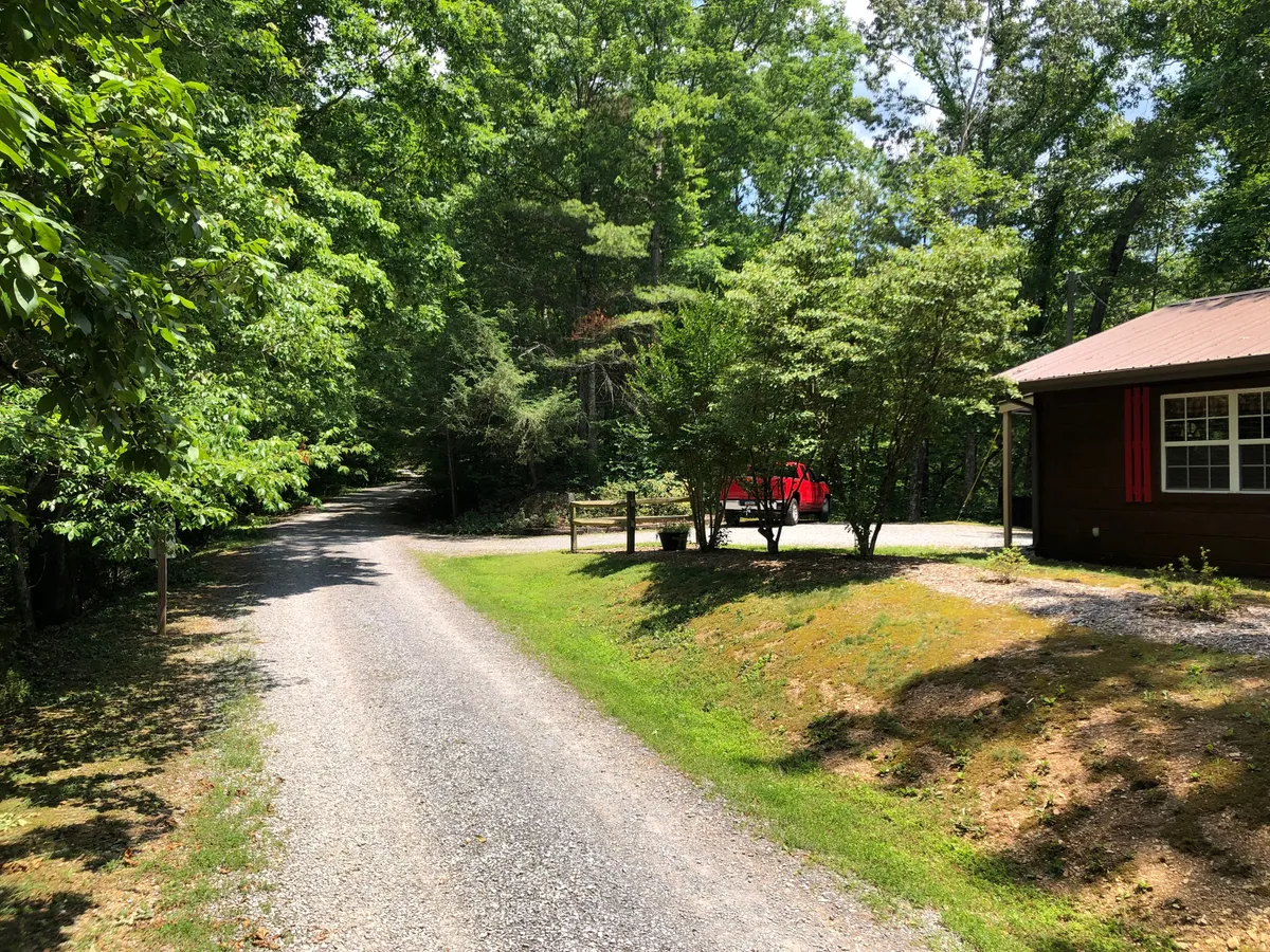 A tranquil exterior path bordered by dense greenery, leading toward a charming house with red accents. The peaceful surroundings evoke the feeling of a secluded mountain escape, emphasizing the connection to nature and opportunity for quiet walks or wildlife spotting.