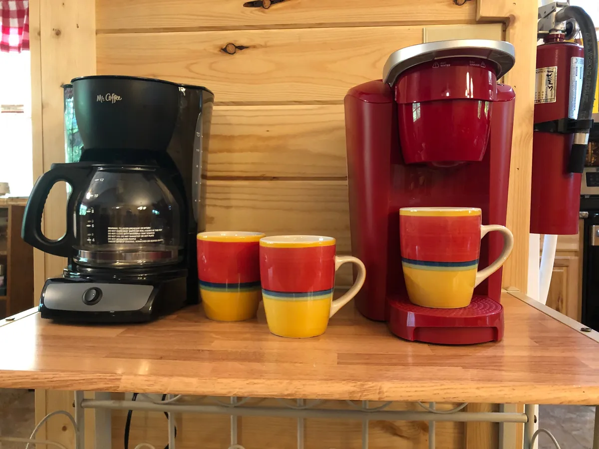 A cozy beverage station featuring a coffee maker, Keurig machine, and an array of colorful mugs. The setup invites guests to prepare coffee and start their day in comfort, reflecting thoughtful amenities.