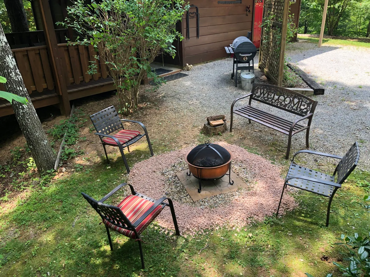 A cozy fire pit area surrounded by comfortable seating and lush greenery, paired with a grill nearby. The communal setup invites families to gather, share stories, and enjoy meals under the stars.