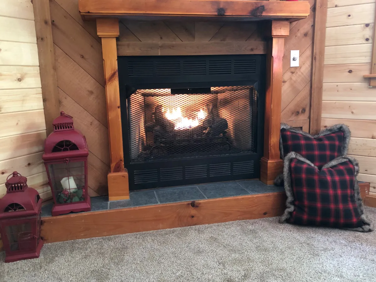 This warm and inviting interior scene centers around a fireplace, with red lanterns and plaid pillows creating a cozy gathering space. Friends or family could easily envision themselves relaxing, chatting, and unwinding together here after a day of activities.