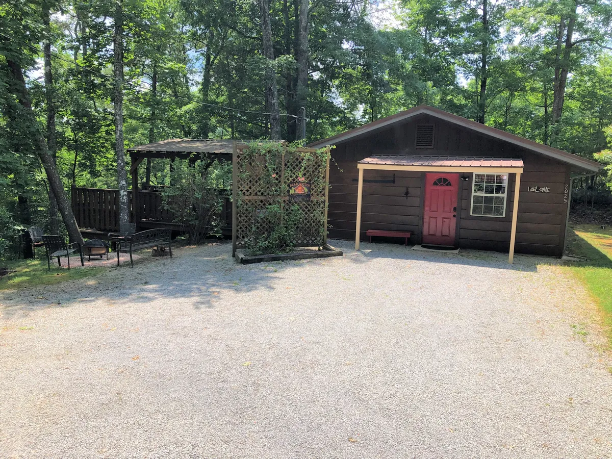 An exterior view of the house with a distinct pink door, lattice structure, and a cozy outdoor seating area. The scene conveys a sense of welcome and relaxation, perfect for unwinding in the garden or stargazing after a day of adventure.