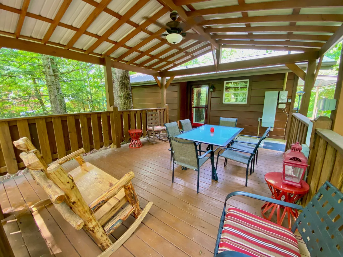 A peaceful outdoor deck furnished with a wooden rocking chair, red accent chairs, a glass table, and surrounded by vibrant greenery. The setup encourages relaxation, outdoor dining, and soaking in the forest atmosphere.