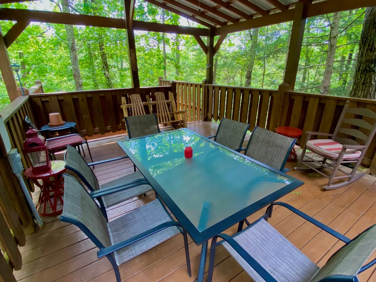A peaceful outdoor deck featuring a glass-top table and wooden chairs, surrounded by lush greenery. The setting is intimate and inviting, ideal for sipping coffee in the morning or enjoying a quiet evening together in nature.