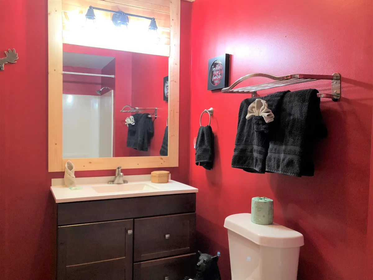The photograph captures a bathroom with rich red walls, a dark wood vanity, large mirror, fresh towels, and decorative wall art. The space feels both stylish and functional, inviting guests to refresh and rejuvenate in private.